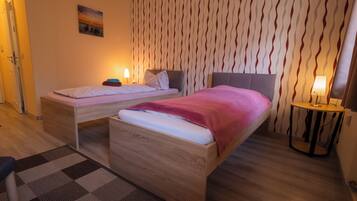 Een hotelkamer met twee bedden, behang met een patroon en een klein tafeltje met een lamp.