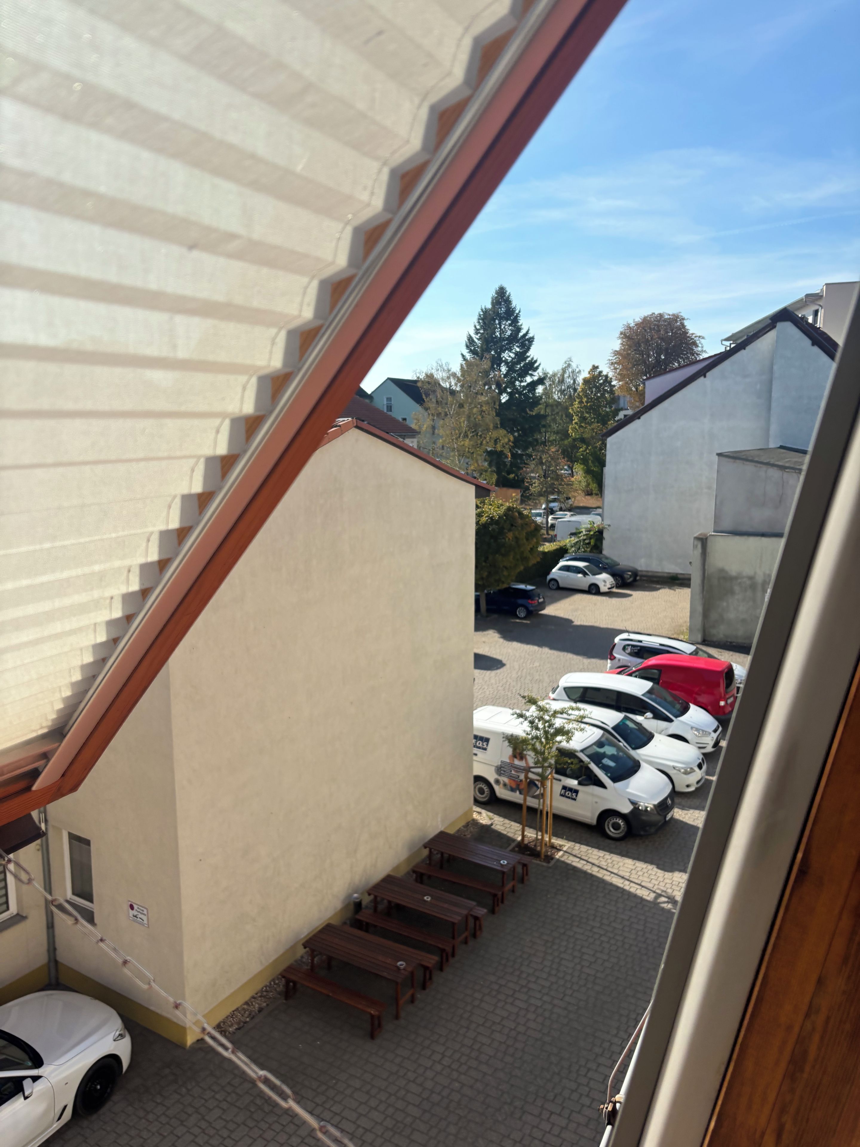 A view from a window overlooking a parking area with several cars, a building with a sloped roof, and a staircase leading to an upper level.