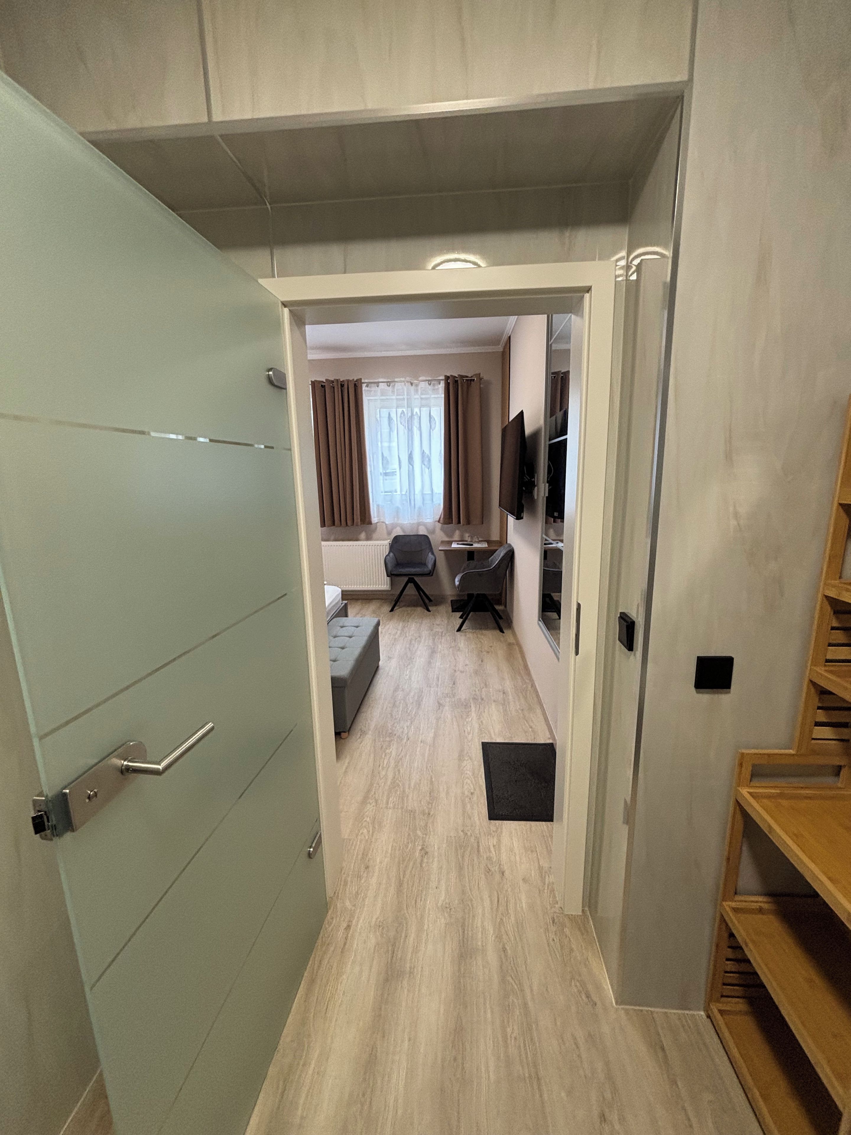 A hallway leading to a bedroom with a bed, a desk, and a chair.