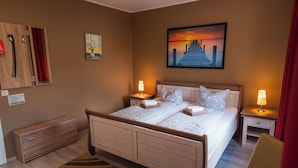Un dormitorio con una cama de madera, dos mesitas de noche con lámparas, un cuadro de una puesta de sol, un armario de madera y una cortina roja.