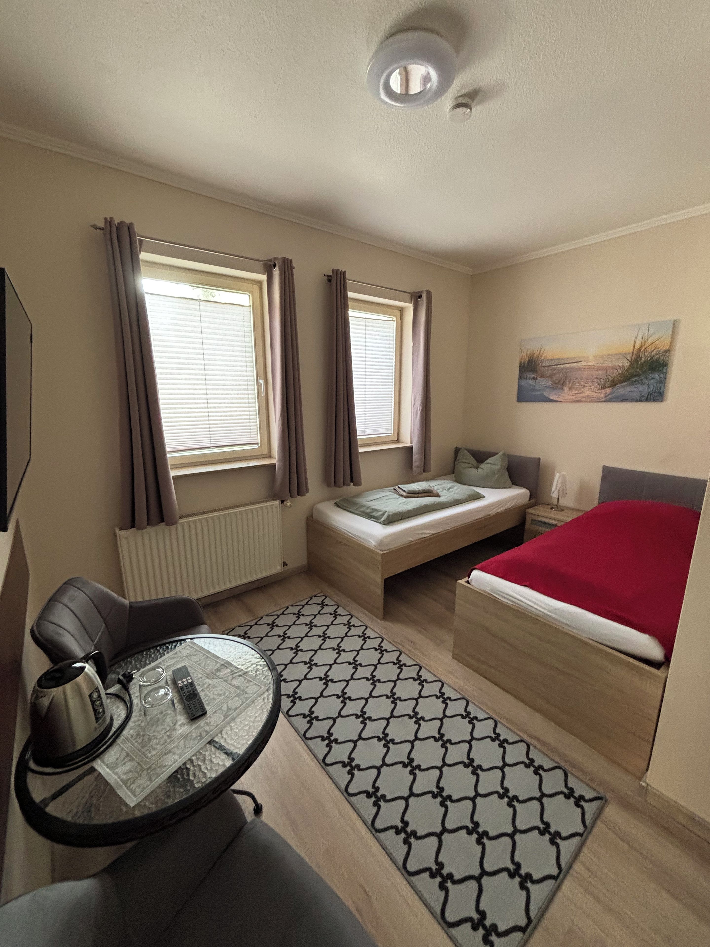 A compact room with a bed, a small table, a chair, and a window with curtains.