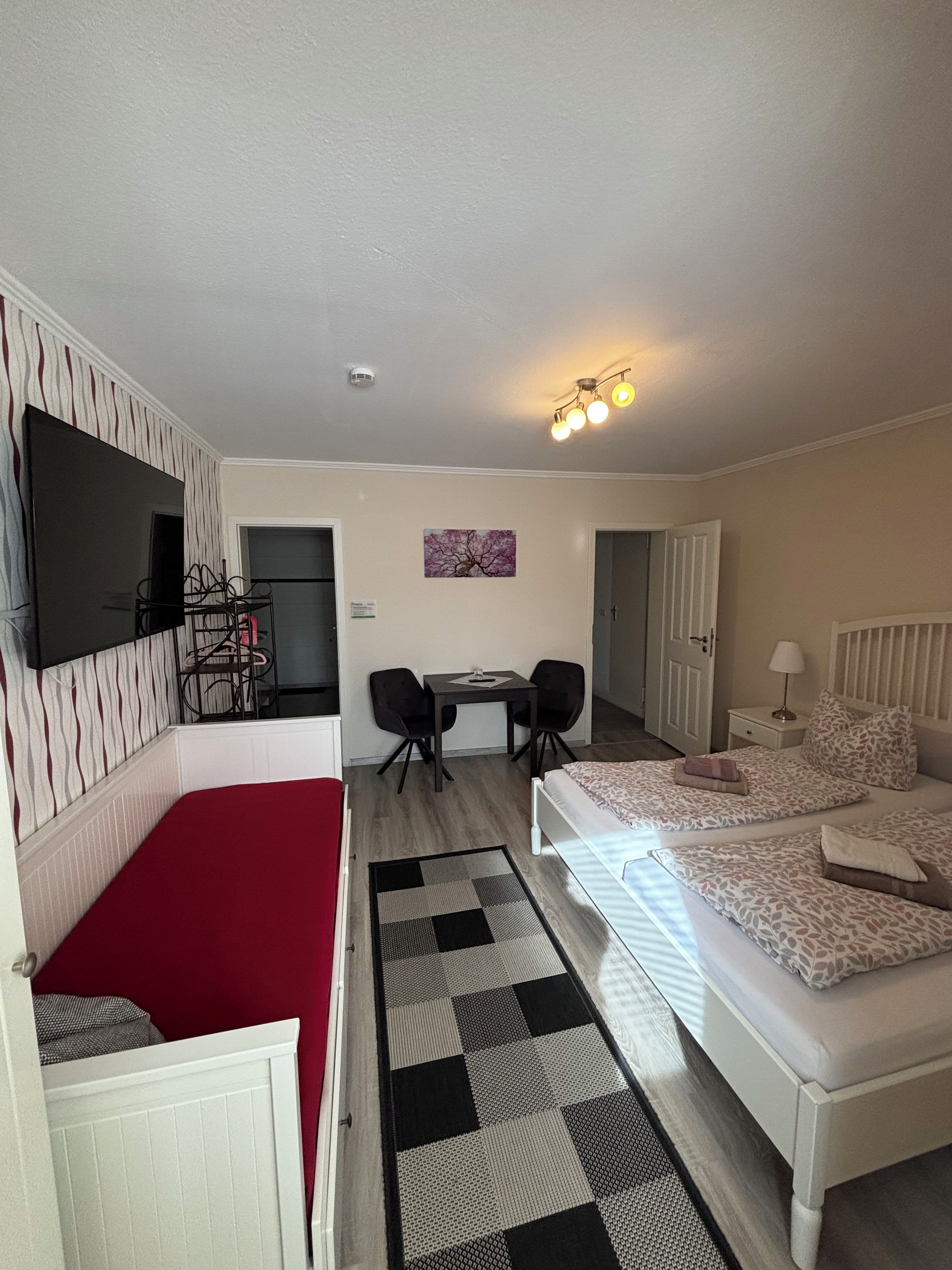 Habitación de hotel con cama, escritorio con dos sillas, televisor y puerta que da a otra habitación.