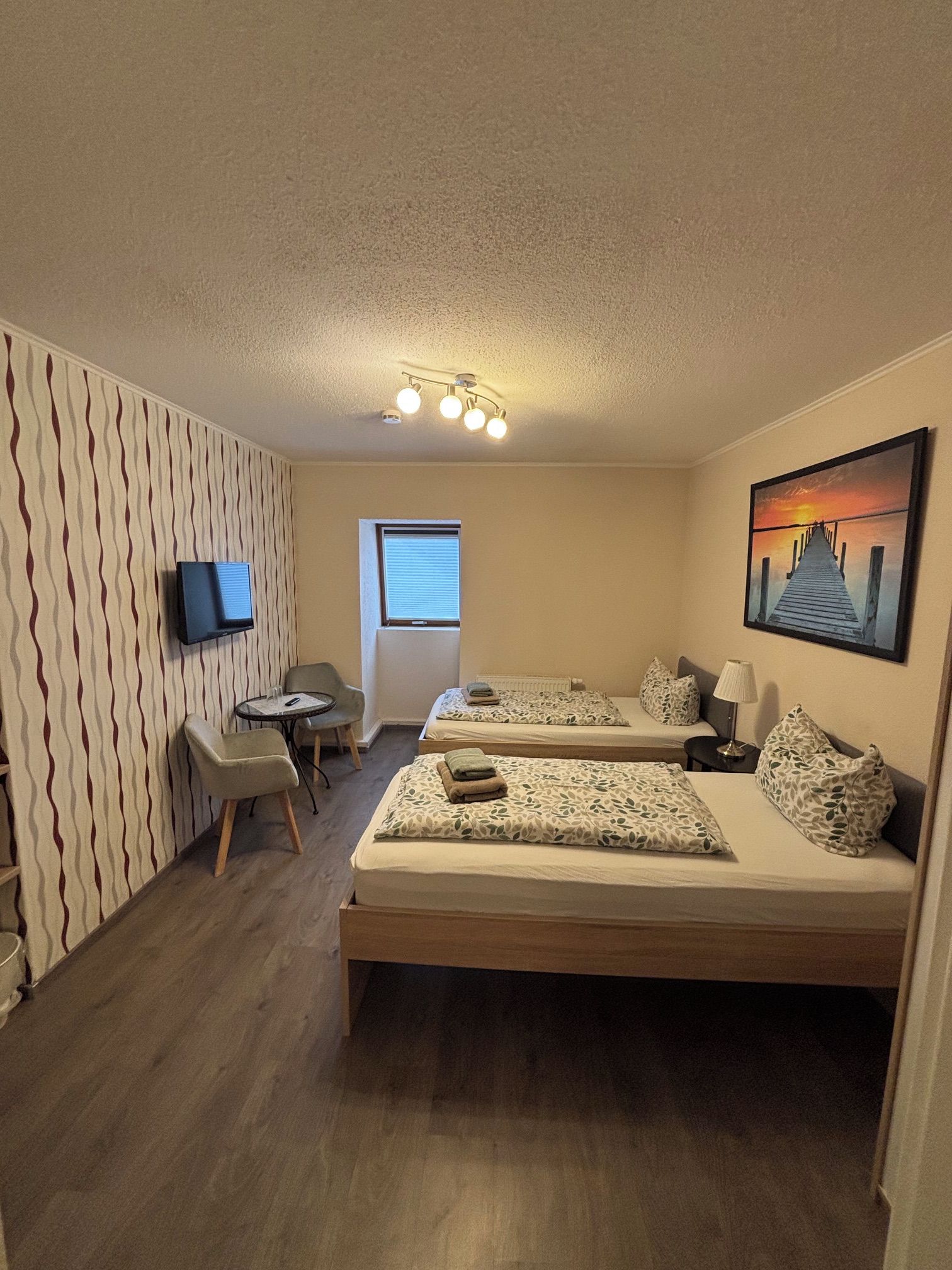 Habitación de hotel con dos camas, televisión, escritorio y ventana.