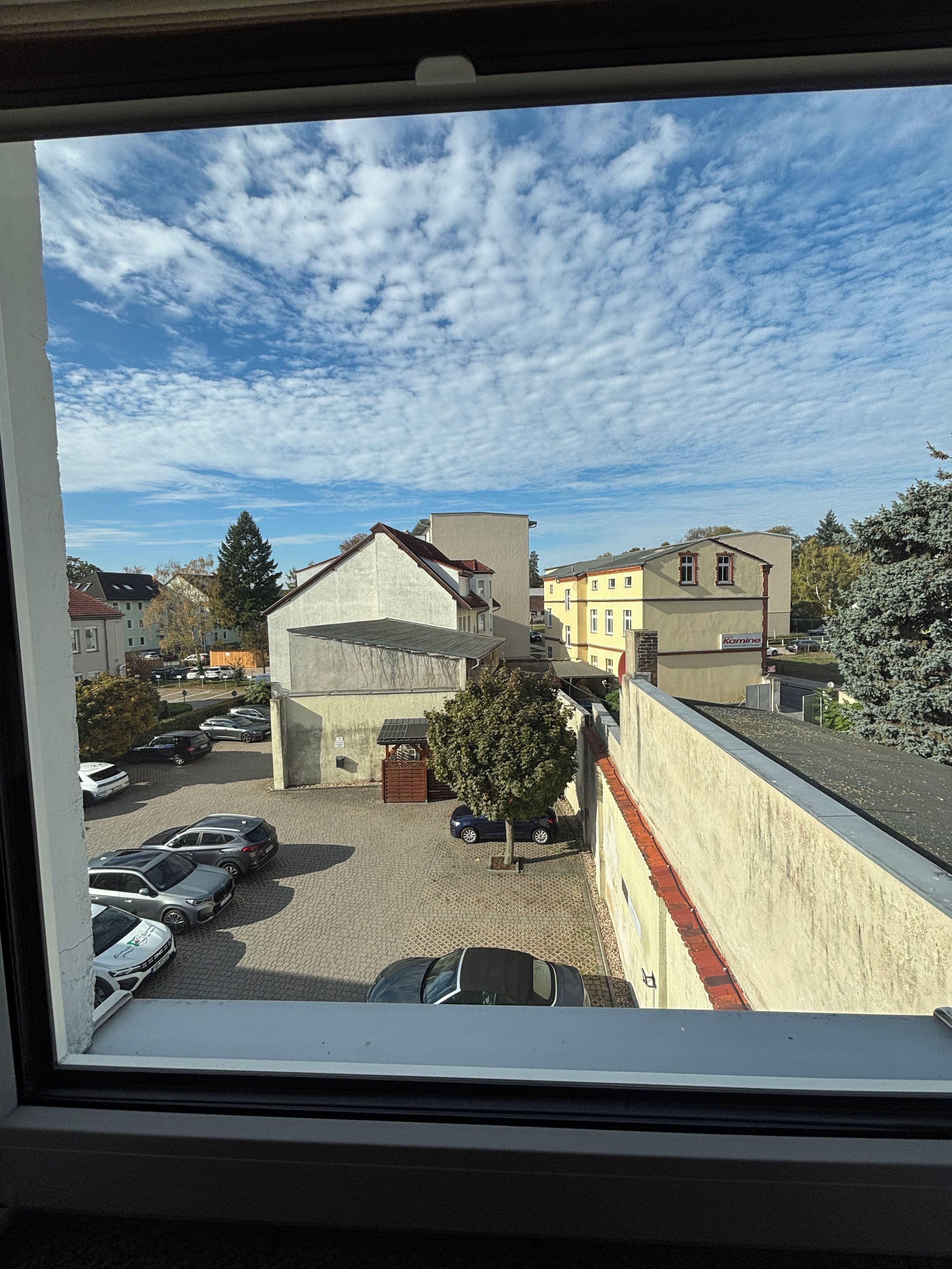 Vista de un estacionamiento con varios autos, un edificio de techo inclinado y un árbol en primer plano.