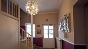 Un pasillo con una escalera, una lámpara decorativa, una puerta y cuadros en la pared.
