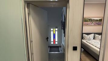 A narrow hallway with a door leading to a room with a bed and a mirror reflecting a room with a bed.