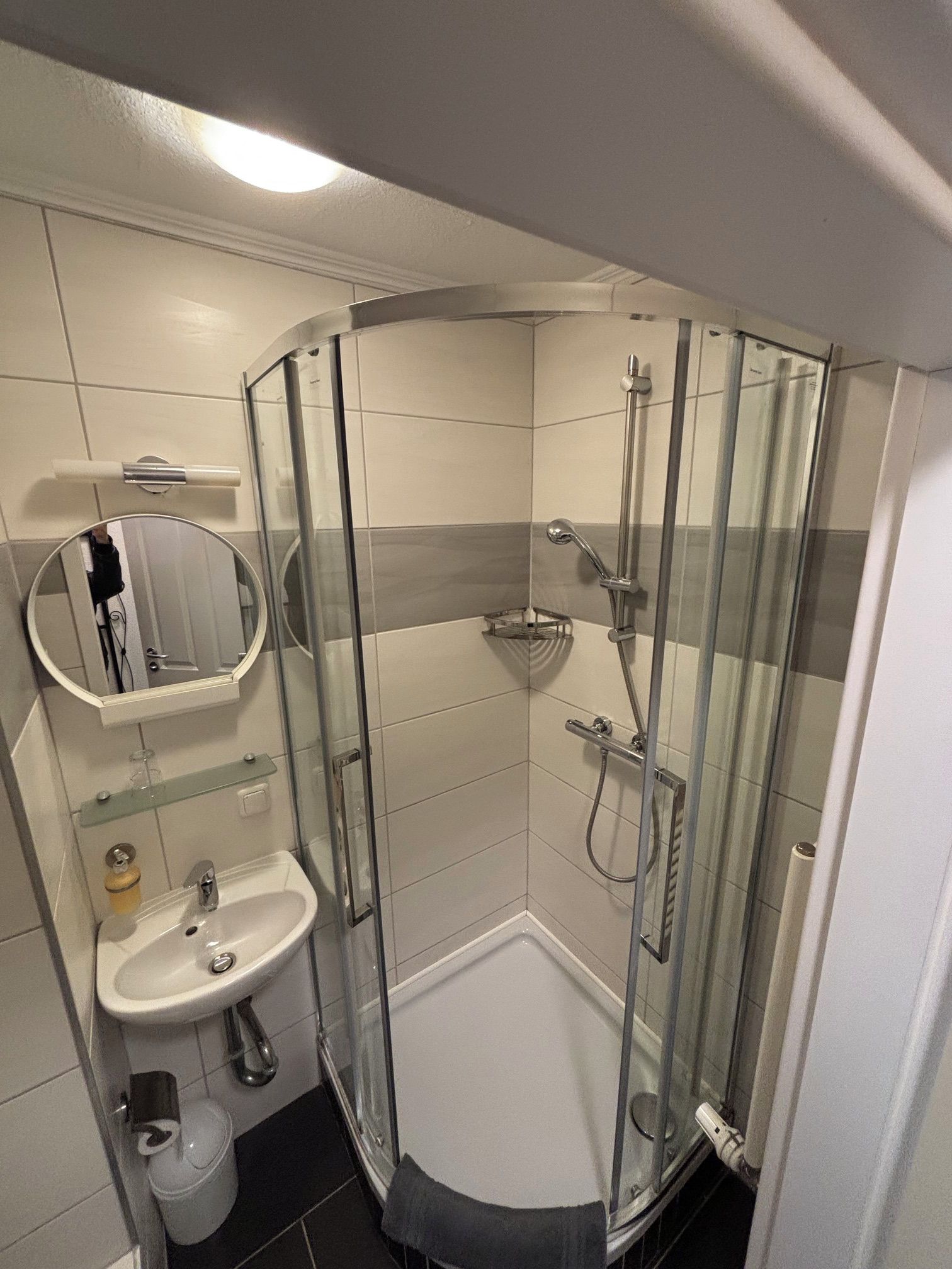 Ein Badezimmer im Eck mit einer Duschkabine, einem Waschbecken, einer Toilette und einem Spiegel.