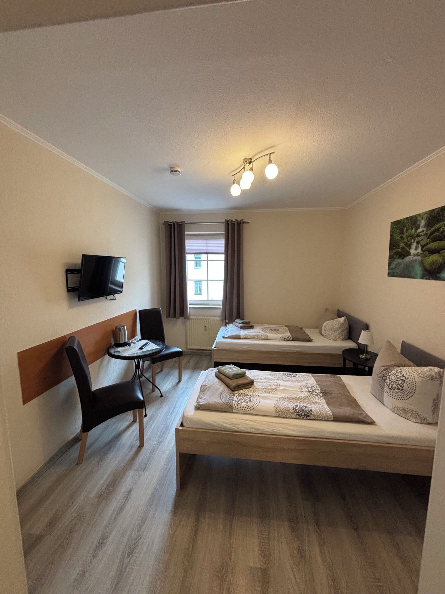 A hotel room with a bed, a desk, a chair, a TV, and a window with curtains.