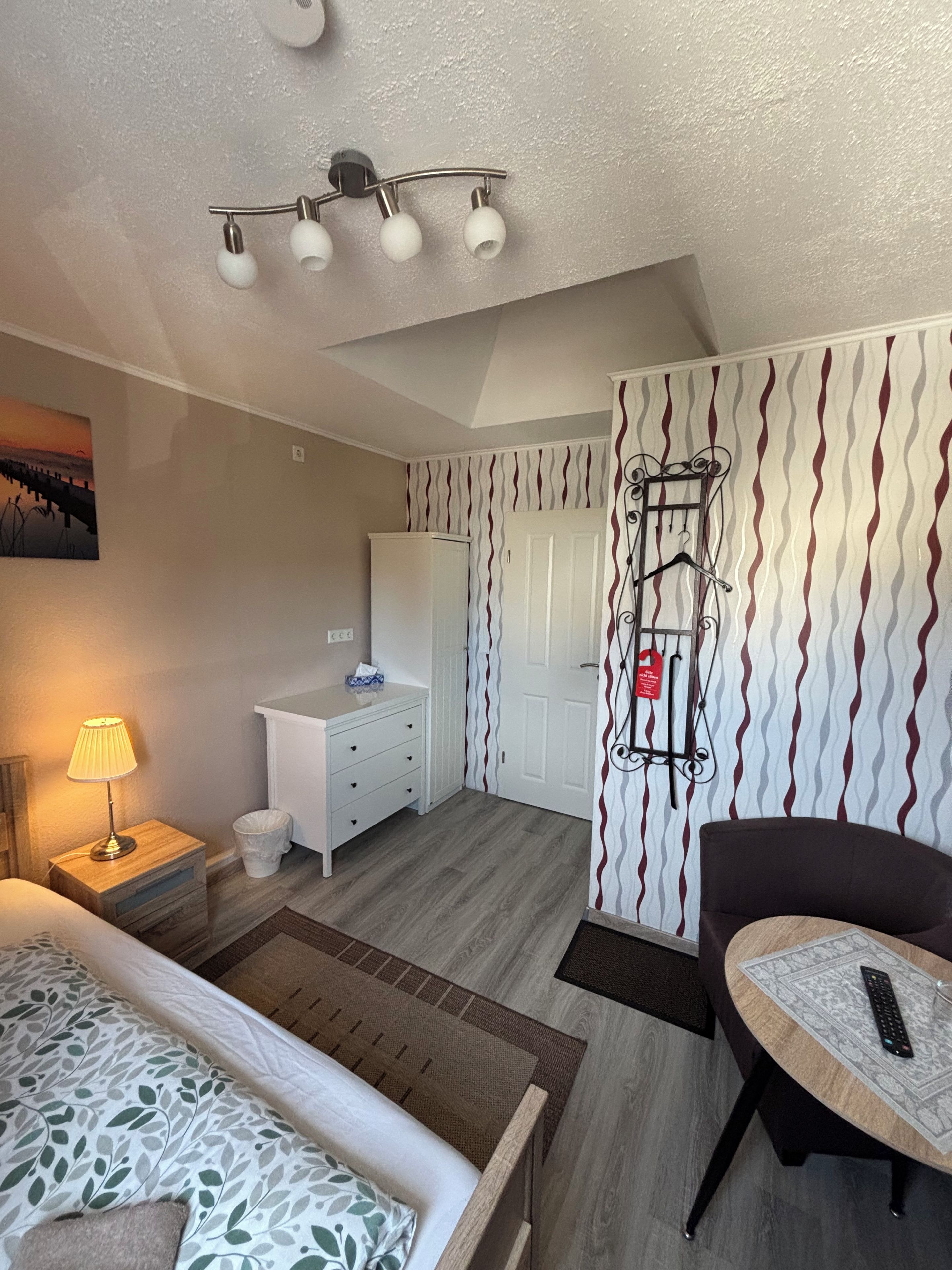 Ett hotellrum med en säng, ett skrivbord, en stol, en lampa, en garderob och en vägg med ett mönster.