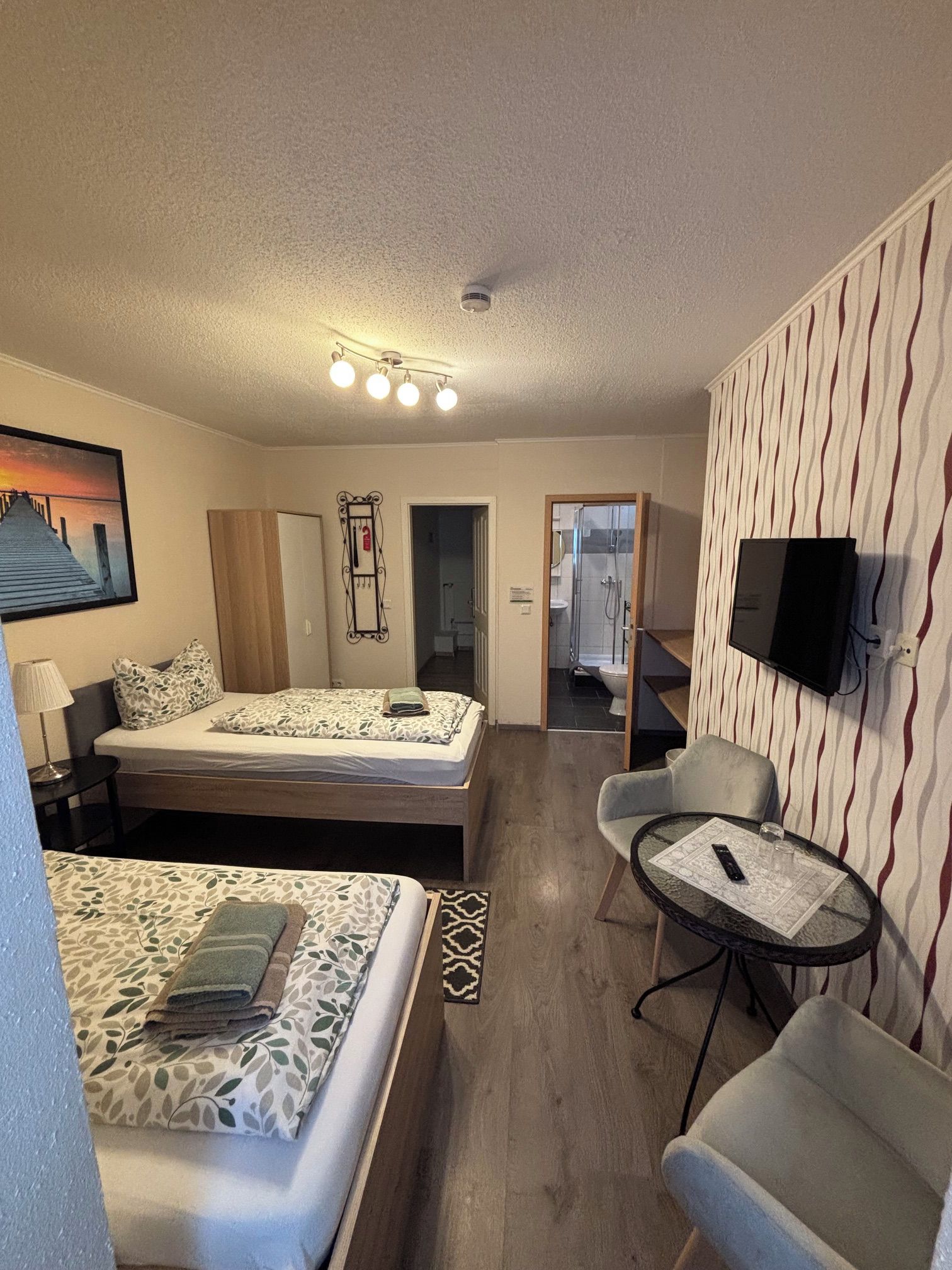 A hotel room with a bed, a desk, a chair, a television, and a bathroom visible through an open door.