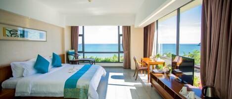 A hotel room with a bed, a desk with a TV, and a view of the ocean.
