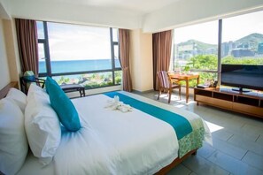 Een hotelkamer met een groot bed, een televisie, een eettafel en uitzicht op de oceaan.