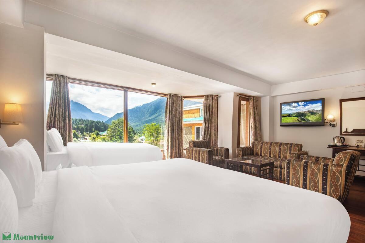 A hotel room with two beds, a sofa set, a TV, and a mountain view.