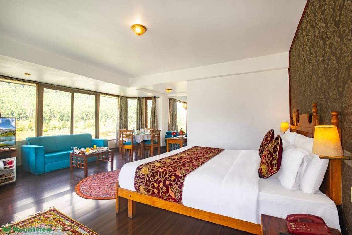 A hotel room with a large bed, a sofa, a dining table, and chairs.