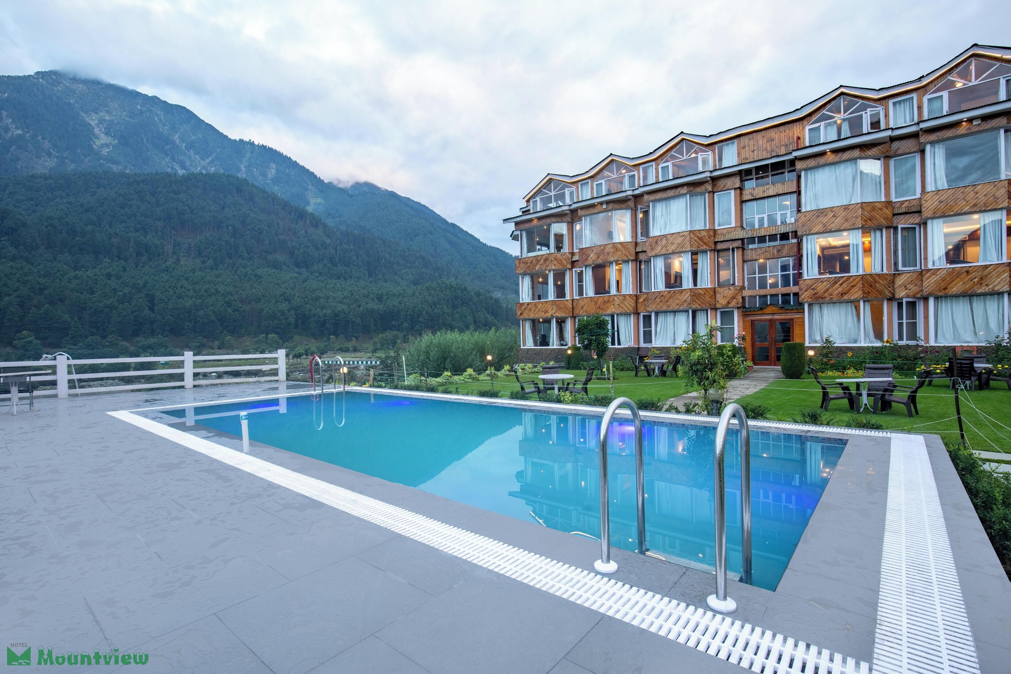 A hotel with a pool, surrounded by mountains and greenery.