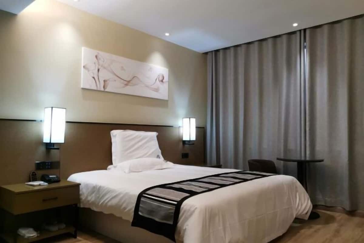 A hotel room with a bed, bedside lamps, a nightstand, a small table, and a painting on the wall.