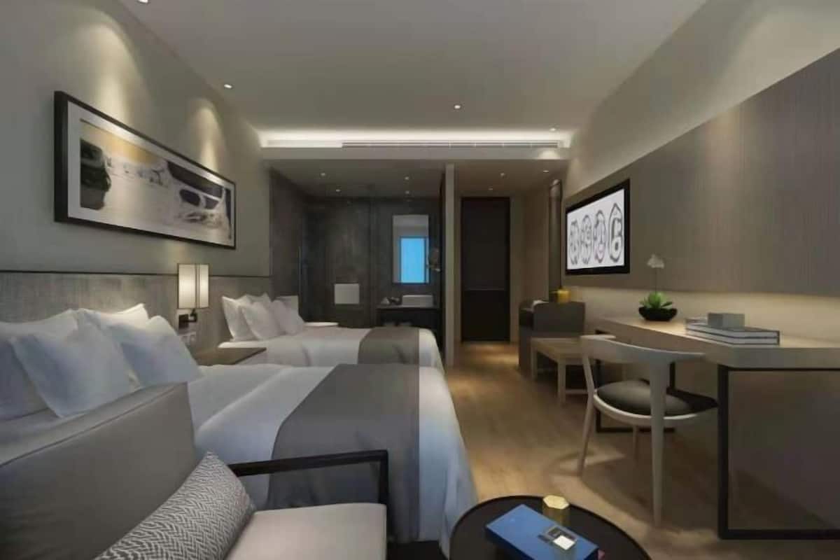 A modern hotel room with two beds, a desk, a chair, and a small table.