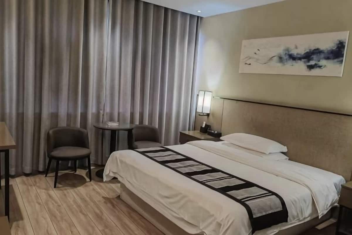 A hotel room with a bed, two chairs, a small table, a nightstand, and a painting on the wall.