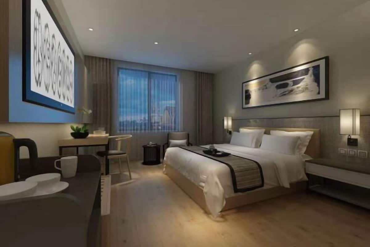 A modern hotel room with a large bed, a desk, a chair, and a window with curtains.
