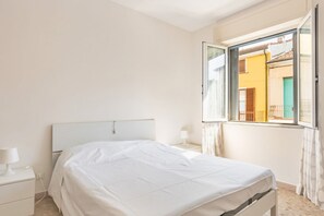 A bedroom with a bed, a nightstand, a lamp, and a window with a view of buildings.