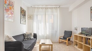 Una sala de estar con sofá, sillón, mesa de centro, televisor y estantería.