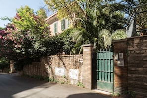 A building with a stone wall, a green gate, and a tree with pink flowers.