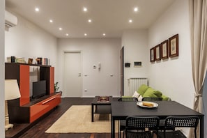 A modern living room with a TV, sofa, dining table, chairs, and artwork on the walls.