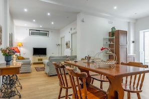 A spacious living area with a wooden dining table, chairs, a sofa, a TV, and a bookshelf. - GuestHost - Spacious 120 sqm apartment in Aci Castello, ideal for 6 people. Features a balcony, private garden, and air conditioning. Aci Castello is a picturesque coastal town in Sicily, famous for its charming Norman castle by the sea. Perfect for thos (Aci Castello)