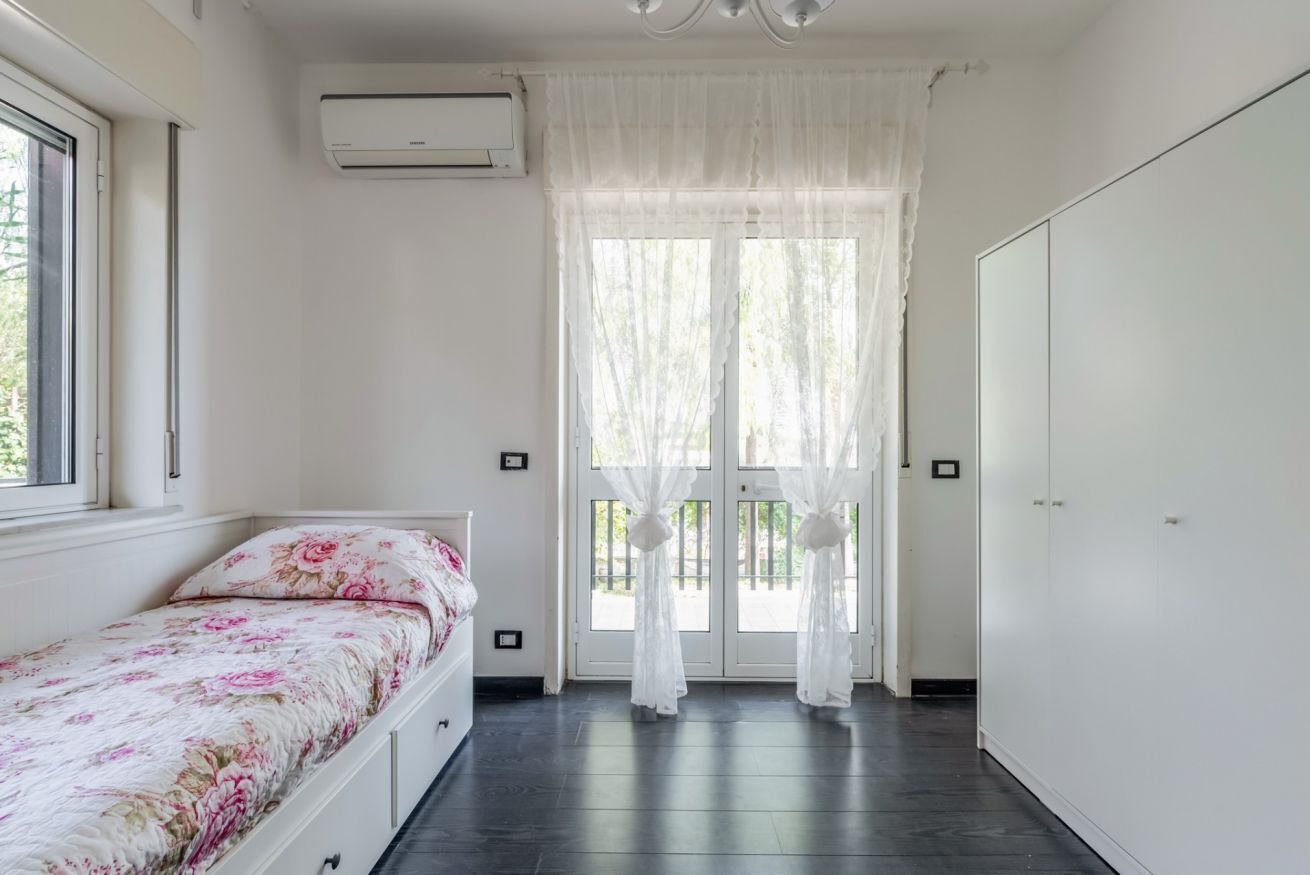 A bedroom with a bed, a window, an air conditioning unit, and a door with curtains.