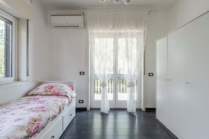A bedroom with a bed, a window, an air conditioning unit, and a door with curtains. - GuestHost - Spacious 120 sqm apartment in Aci Castello, ideal for 6 people. Features a balcony, private garden, and air conditioning. Aci Castello is a picturesque coastal town in Sicily, famous for its charming Norman castle by the sea. Perfect for thos (Aci Castello)