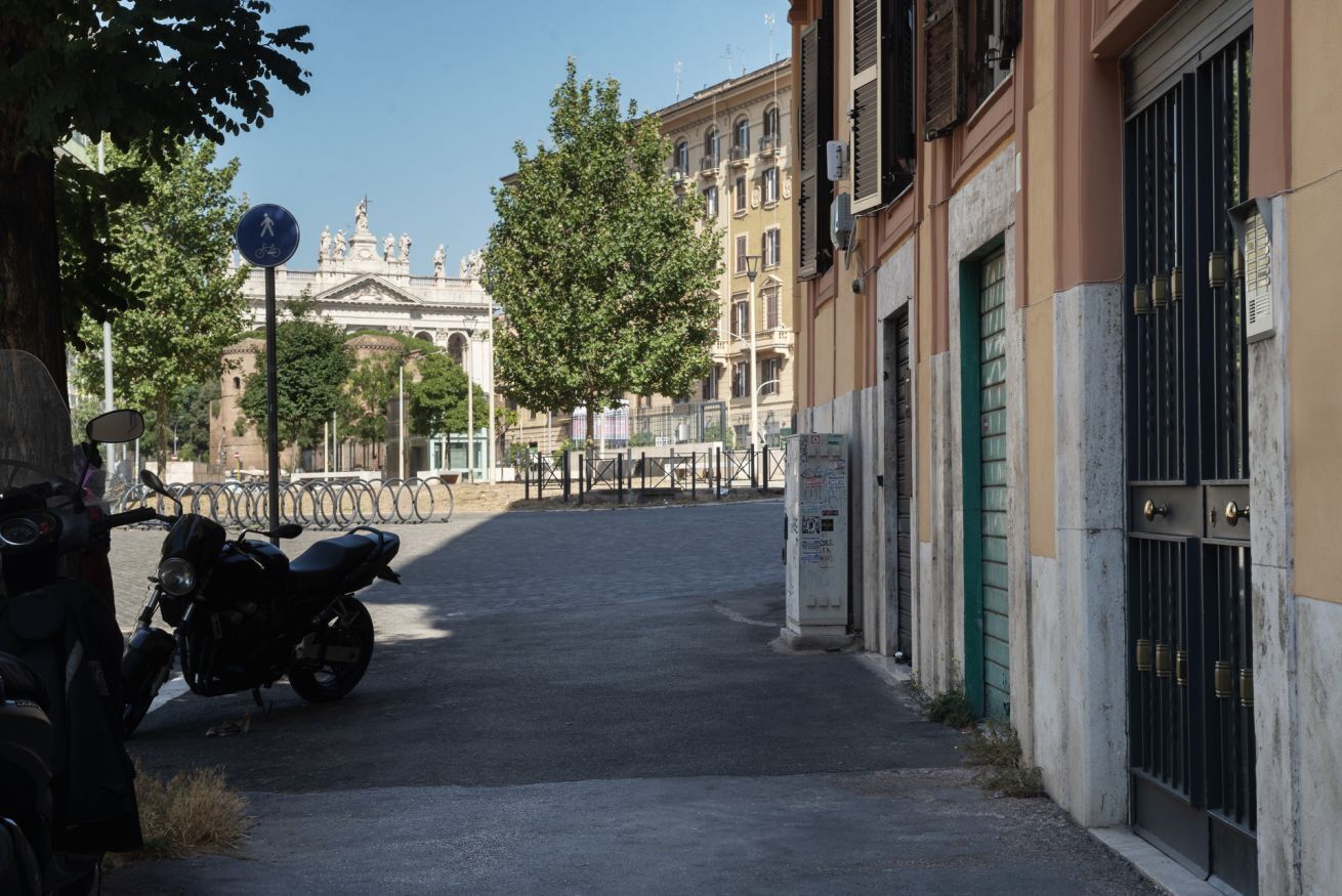 Una calle con una motocicleta estacionada al lado, una señal de carril para bicicletas y un edificio con entrada protegida por una reja.