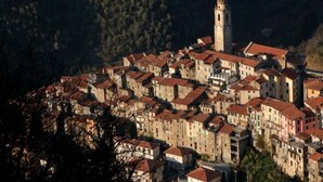 A historic town with a prominent tower, closely packed buildings, and a mountainous backdrop.