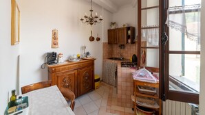 A compact kitchen with a dining area, a chandelier, and a window with lace curtains.