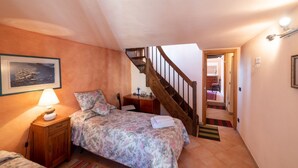 A bedroom with a bed, a nightstand, a lamp, a framed picture, a wooden staircase, and a door leading to another room.