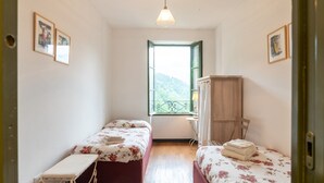 Eine kleine, einfache Unterkunft mit zwei Betten, einem Holzschrank, einem Fenster mit Ausblick und einer Pendelleuchte.