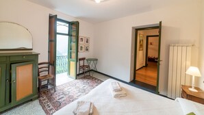 Ein Schlafzimmer mit einem Bett, einem Schreibtisch, einem Sessel, einem kleinen Tisch und einer Tür zu einem anderen Raum.