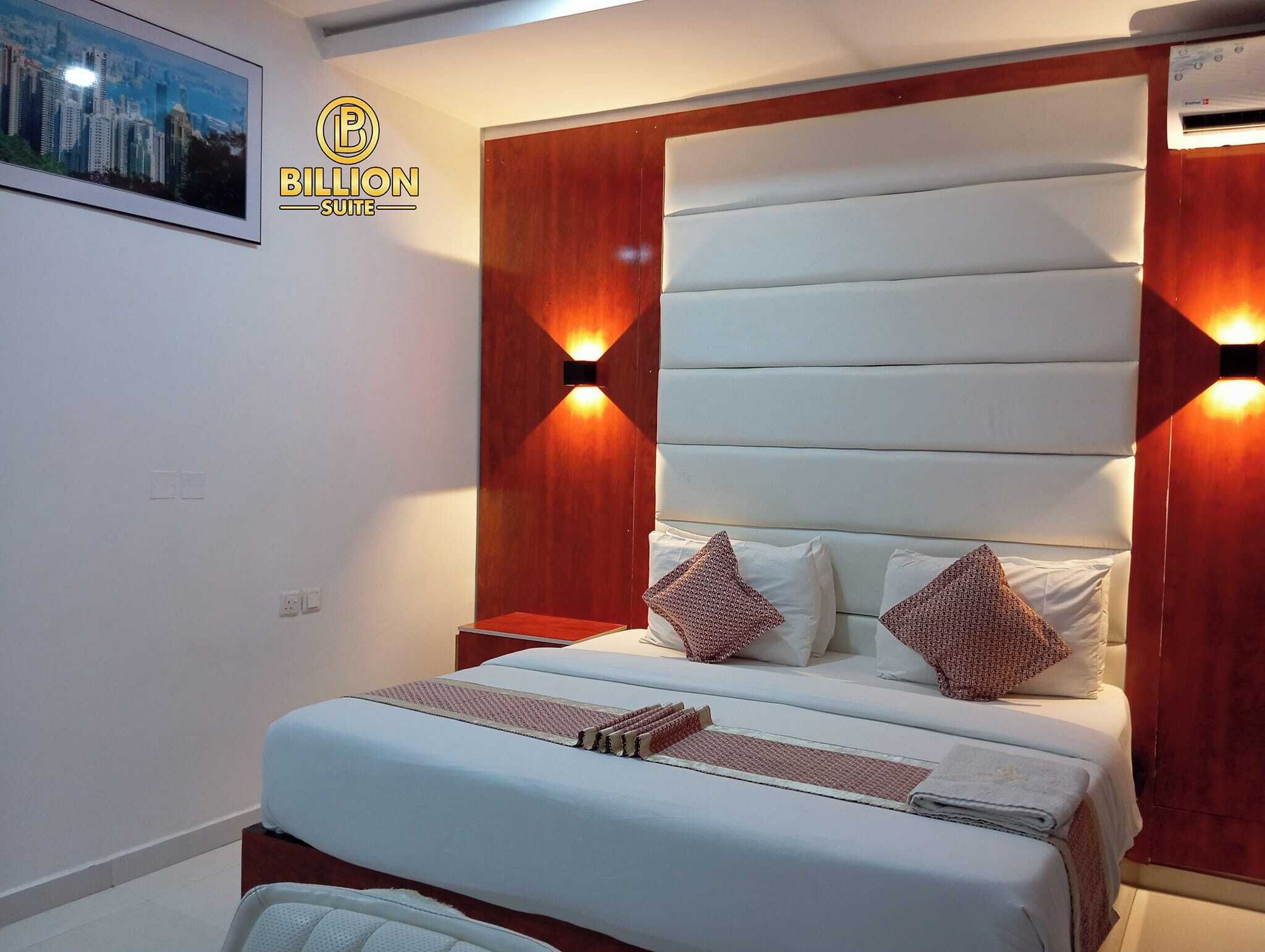 A modern bedroom with a large bed, wooden headboard, and two wall-mounted lights.
