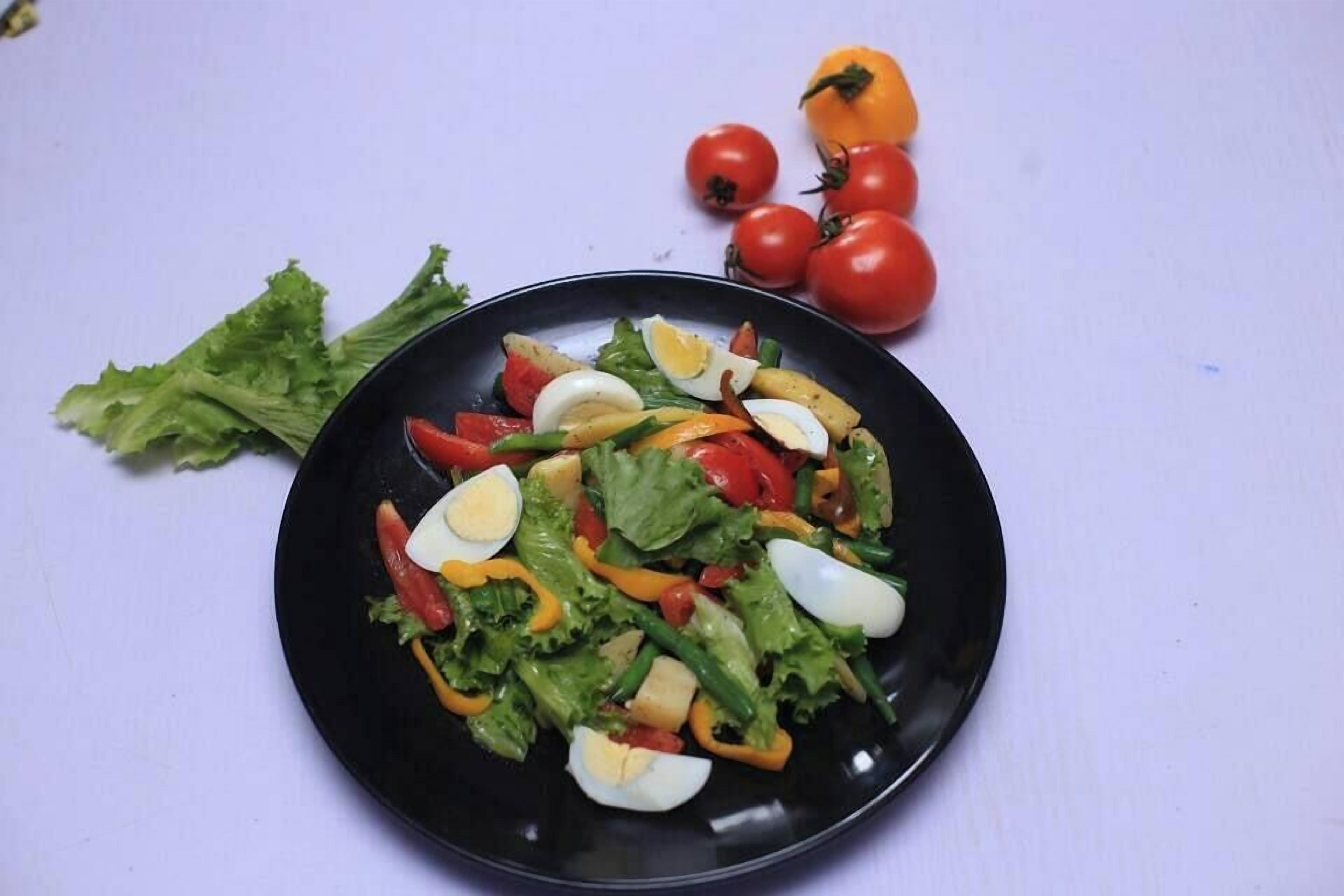 Une assiette noire contenant une salade composée de laitue, de tomates, de poivrons et d’œufs.