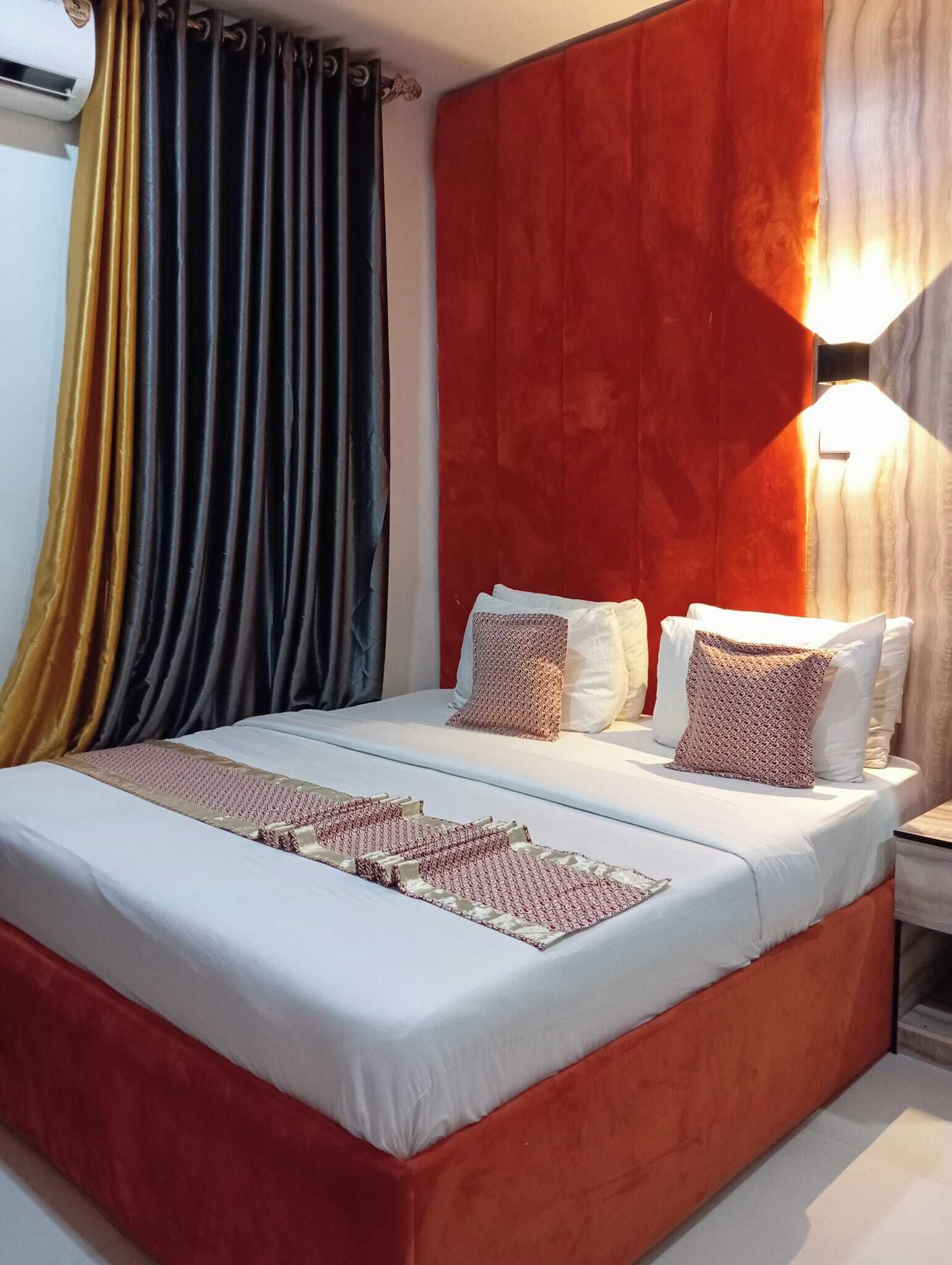Une chambre d’hôtel avec un lit, des rideaux, une table de chevet et une lampe fixée au mur.