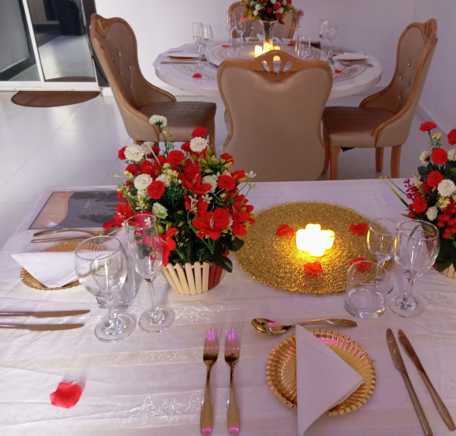 A dining table set with white tablecloth, gold plates, and clear glassware.