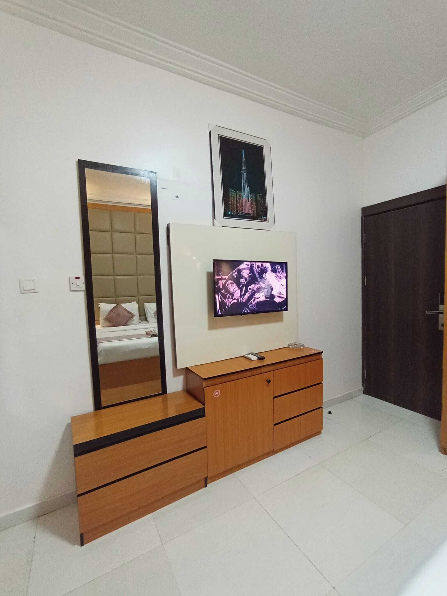 A bedroom with a bed, a dresser, a TV, a mirror, and a door.
