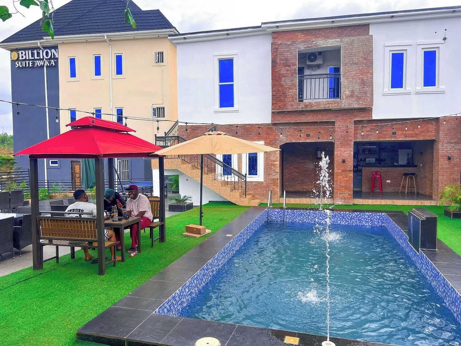 A pool area with a fountain, a covered seating area, and a building labeled "Billion Suite Tawka".