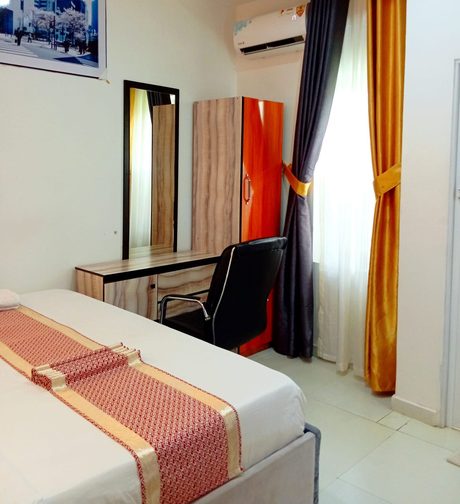 A hotel room with a bed, a desk, a chair, a mirror, and a window with curtains.