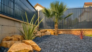 Ein angelegter Garten mit Steinen, einer Palme und einem Zaun.