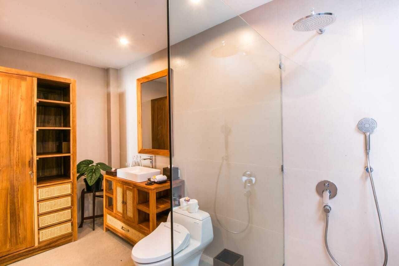 A modern bathroom with a glass shower enclosure, a wooden cabinet with drawers, a sink, and a toilet.
