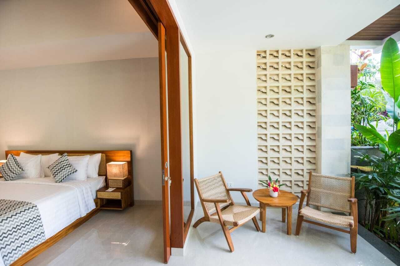 A bedroom with a bed, bedside tables, a nightstand, a chair, a small table with a vase, and a wall with a patterned design.