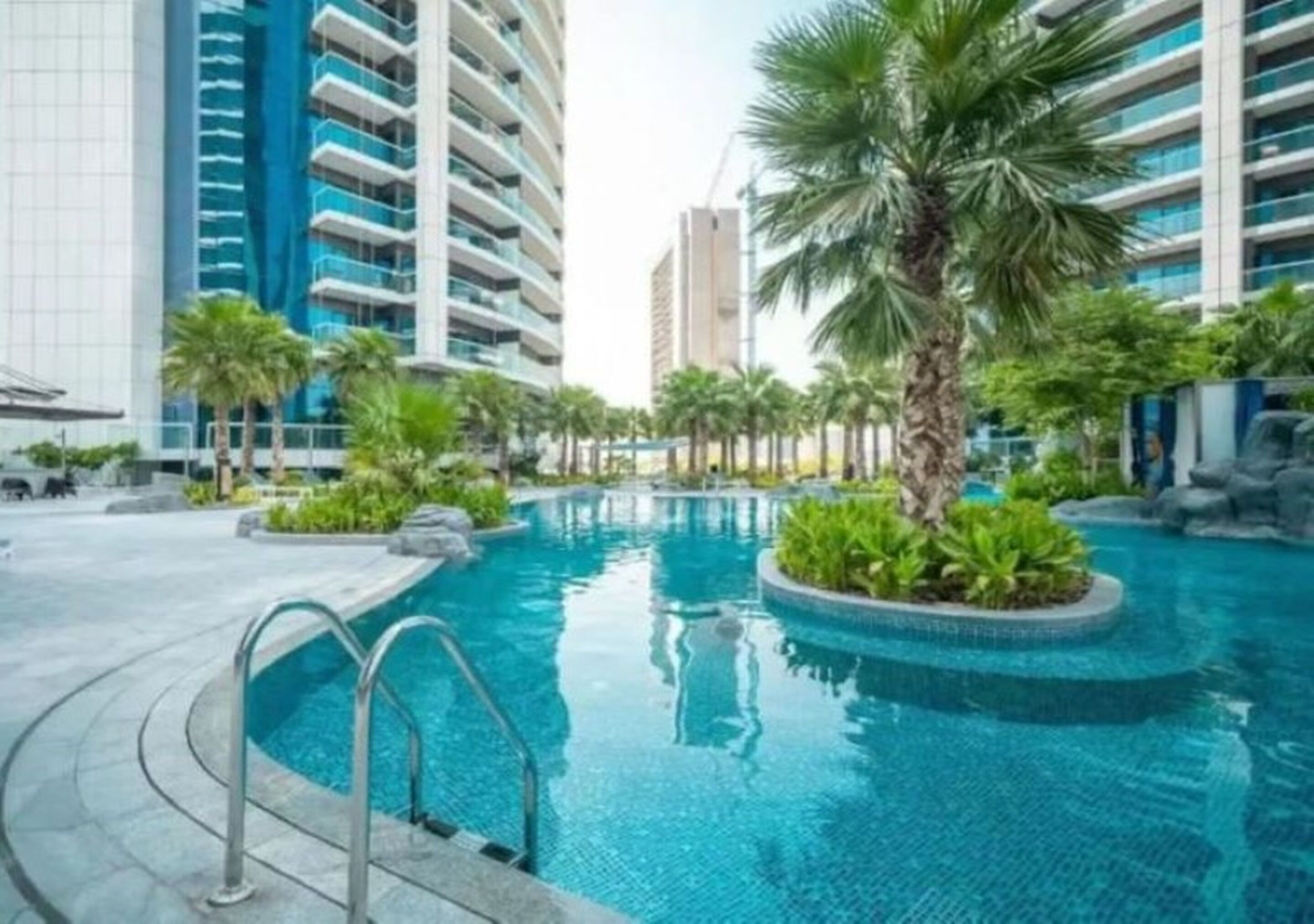A swimming pool surrounded by palm trees and modern buildings.