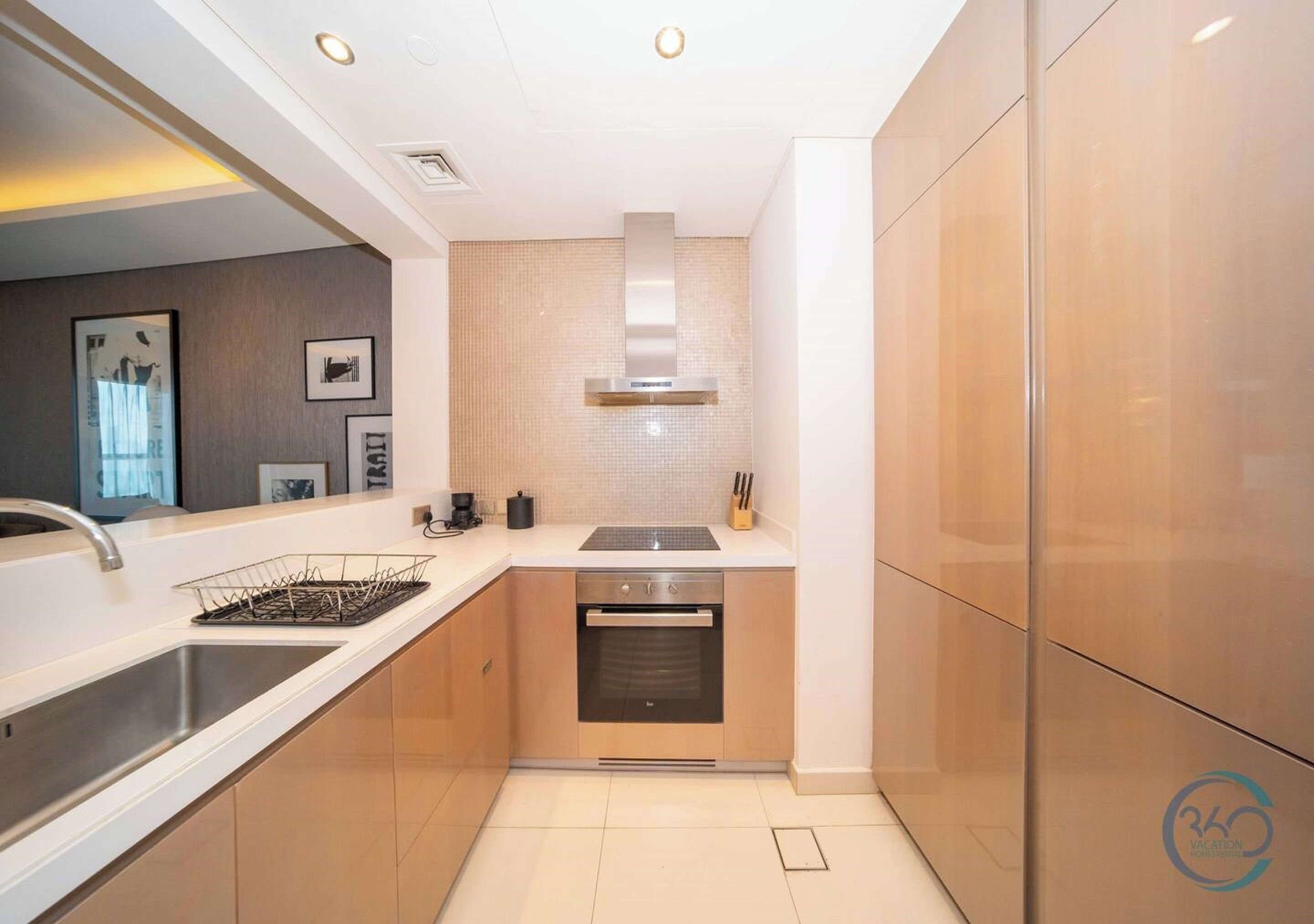 A modern kitchen with a stainless steel sink, a built-in oven, and a microwave. There is a white countertop and wooden cabinets.
