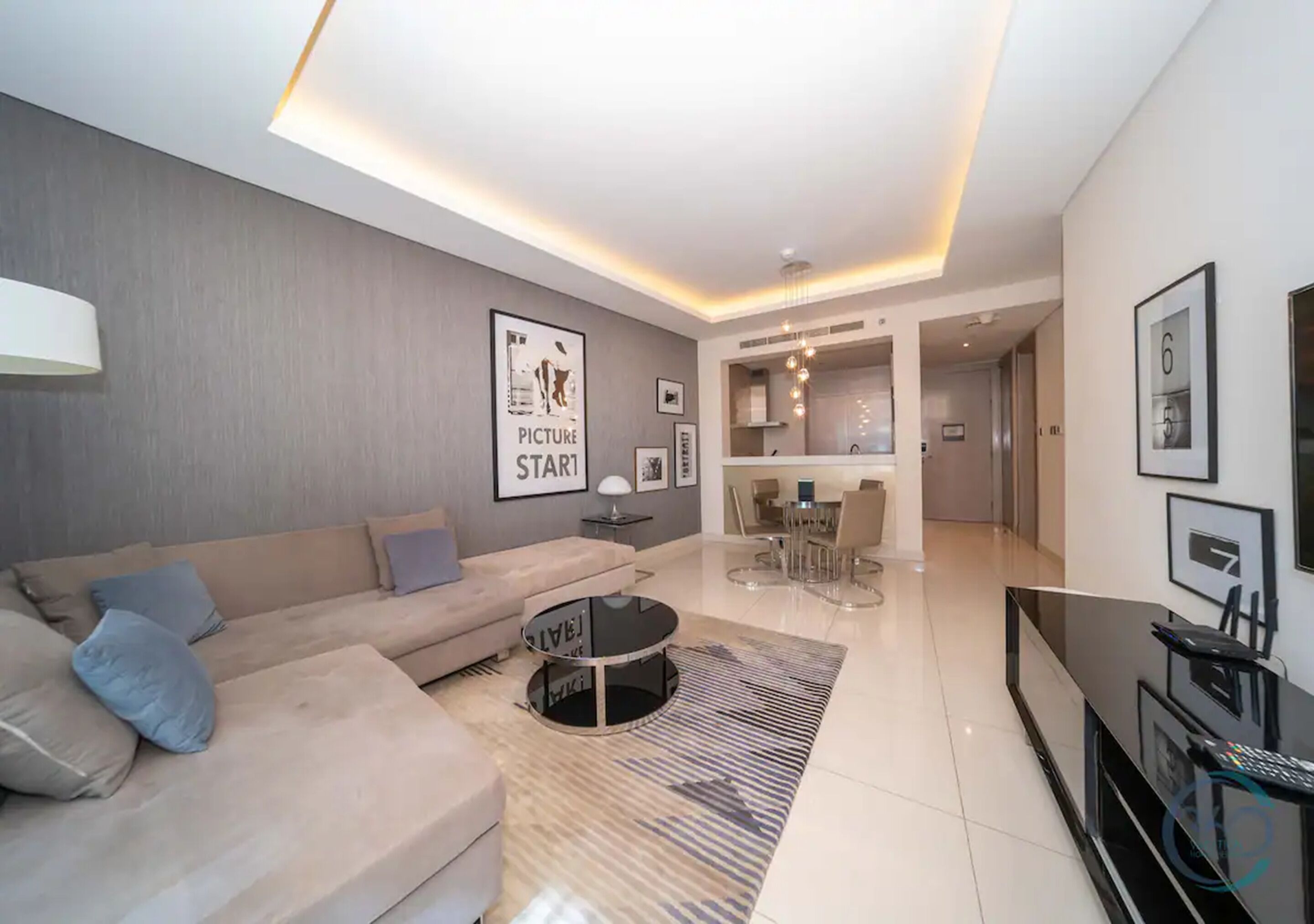 A modern living room with a sofa, coffee table, and TV. There is a dining area with chairs and a table.
