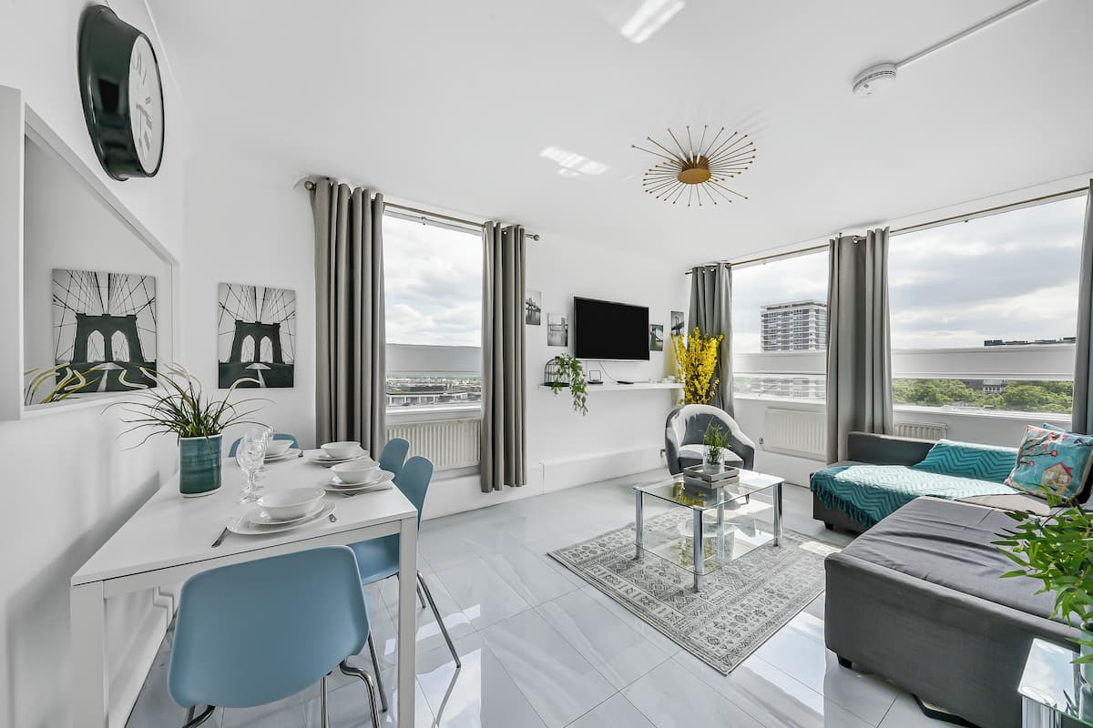 A modern living room with a dining area, large windows, a flat-screen TV, and a city view.